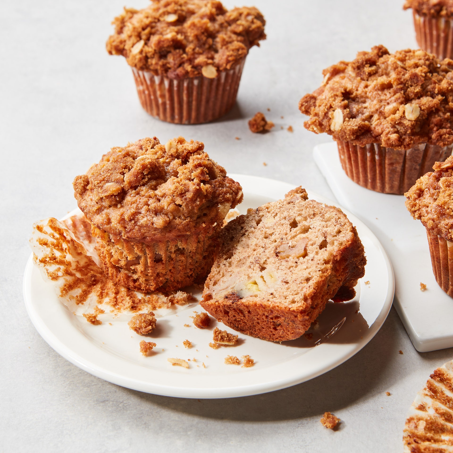 A plate of banana nut muffins with brown sugar streusel being sliced in half.