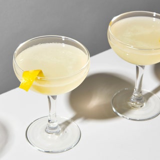 Photo of three glasses of a Bee's Knees cocktail in coupes with lemon peel garnishes.
