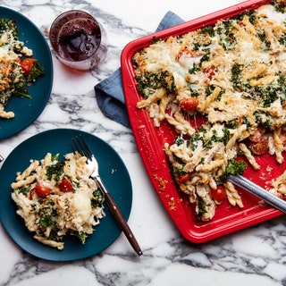 Chicken pasta bake on a red sheet pan next to two blue plates.