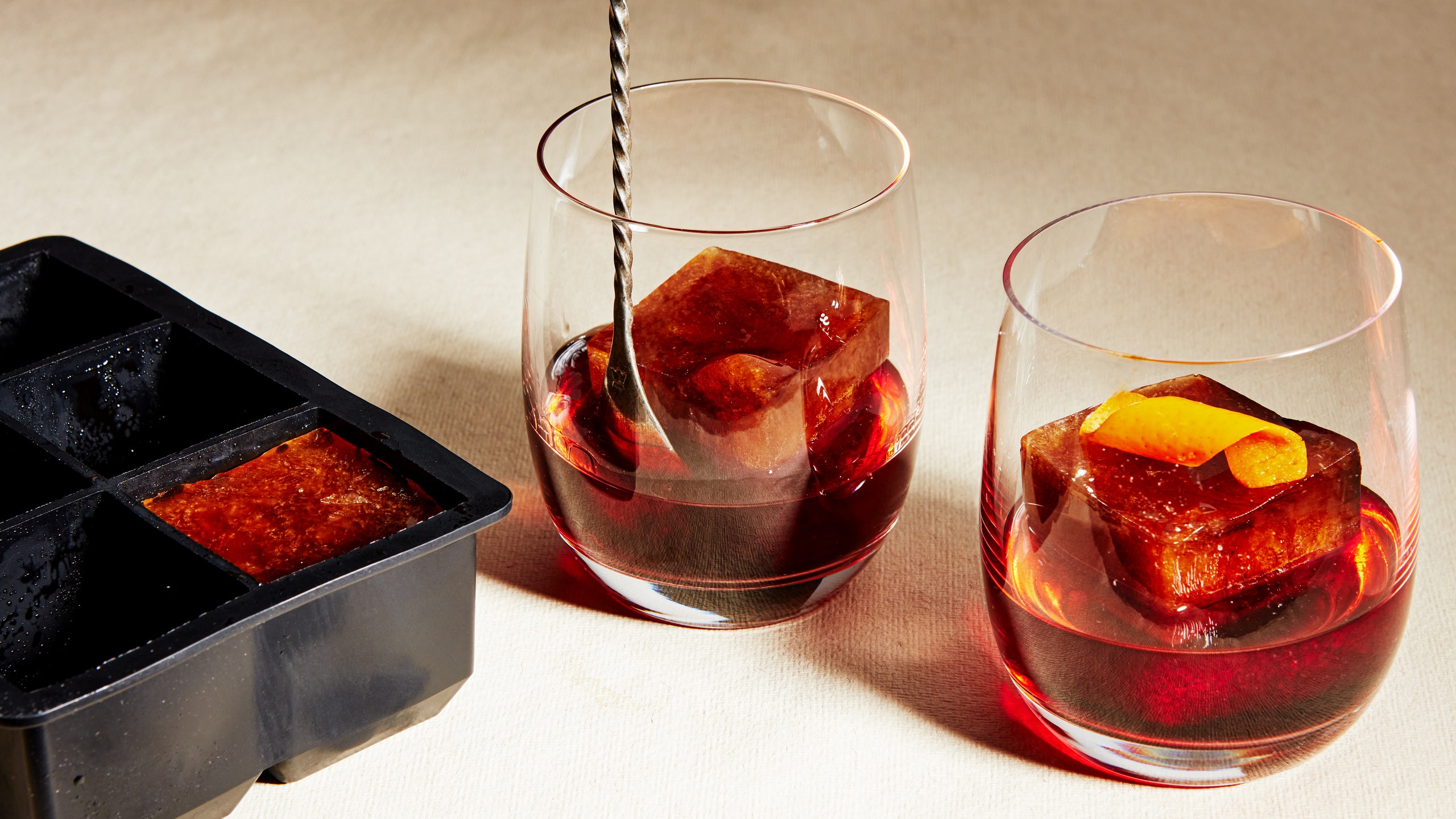 An ice tray with a coffee ice cube alongside two coffee negronis.