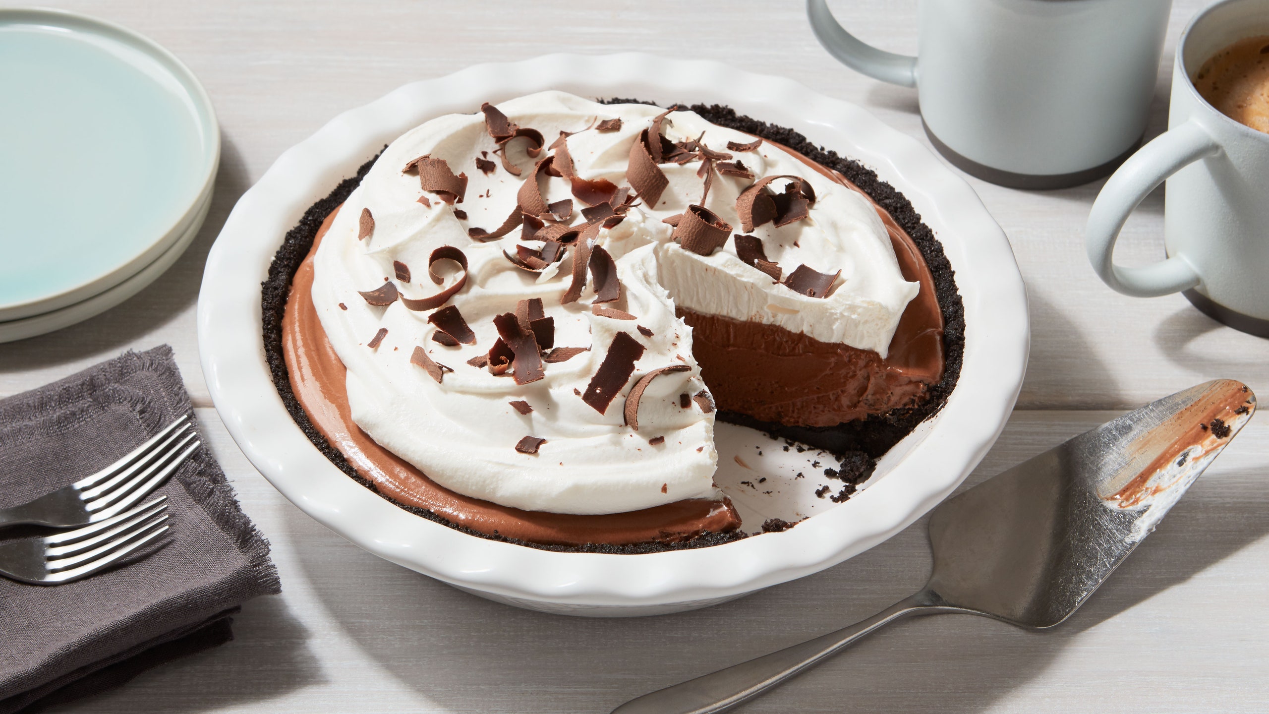 A pie of chocolate filling on a Oreo cookie crust topping with whipped cream and chocolate shavings.