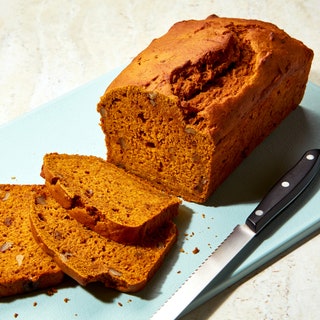 A loaf of pumpkin bread made with cider and filled with chopped walnuts on a cutting board with a serrated knife.