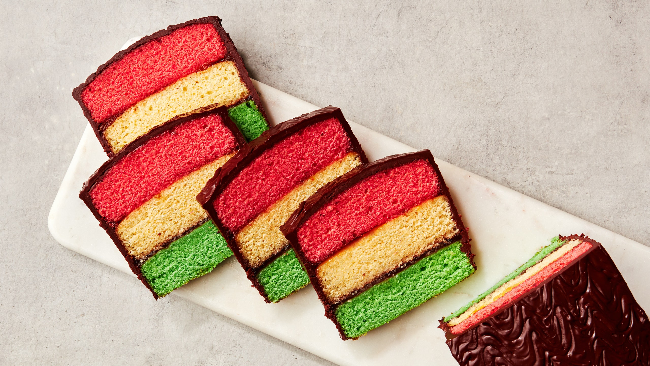 A rainbow cookie cake on a platter cut into slices.