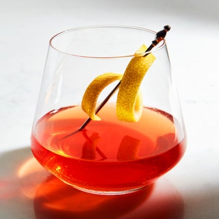 Classic Sazerac cocktail in a glass made with rye whiskey and Herbsaint garnished with a lemon peel on a cocktail pick.