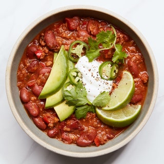 Ground turkey with kidney beans and diced tomatoes in a bowl topped with sour cream avocados slices cilantro lime wedges...